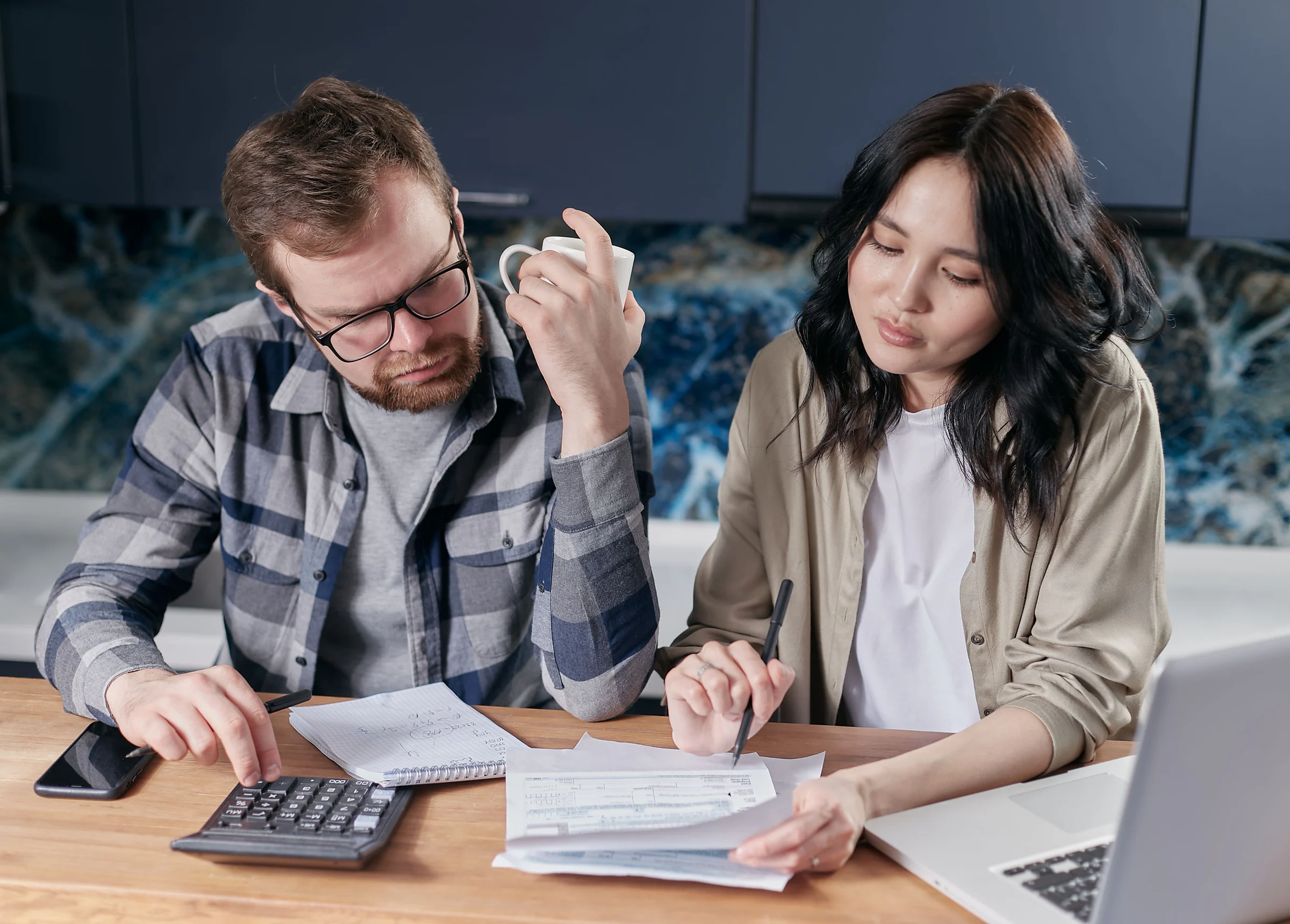 Hai người cùng xem hóa đơn, máy tính và tài liệu ngân sách gia đình bên cạnh máy tính xách tay.