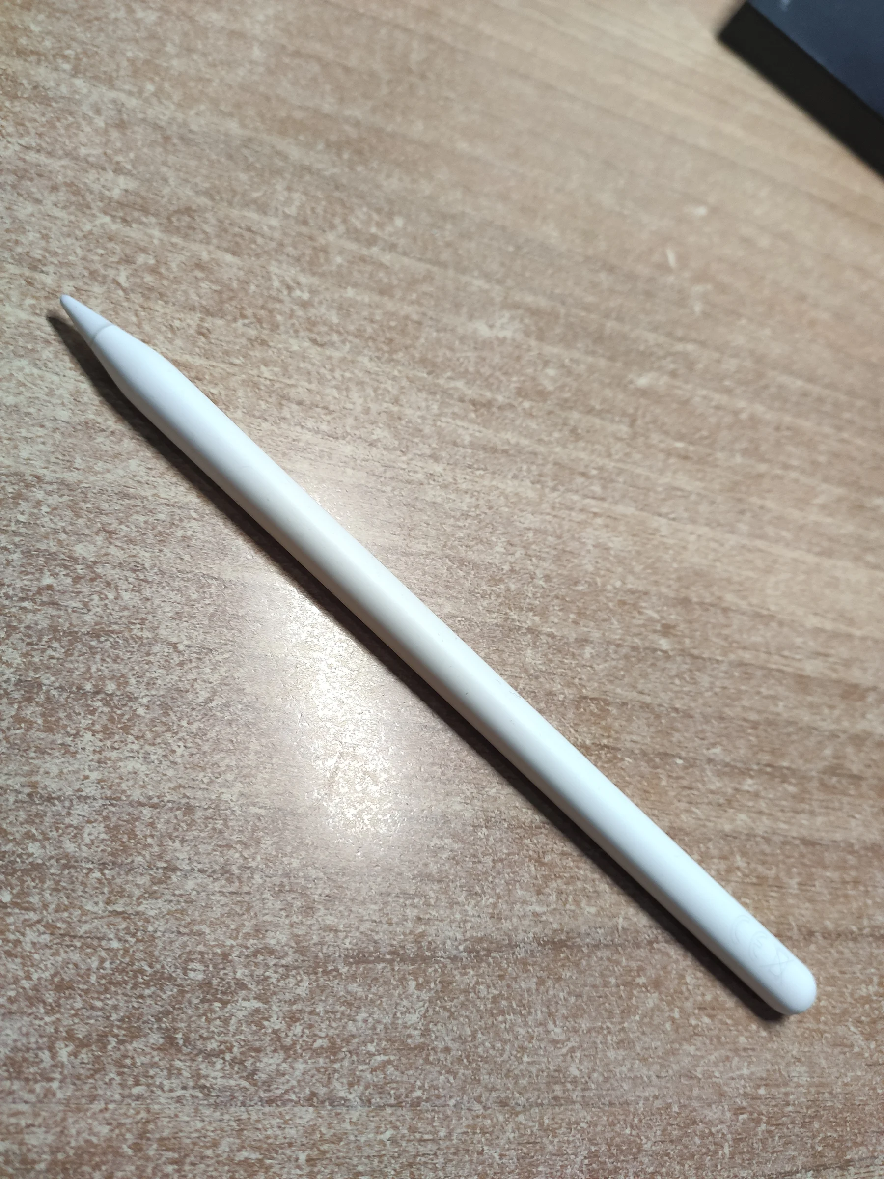 Apple Pencil nằm chéo trên mặt bàn gỗ, nhìn rõ toàn bộ thân và đầu bút