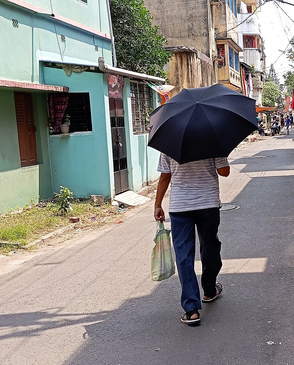 Một người đàn ông cầm ô đi trên phố, minh họa trạng thái cầm hoặc che ô với 着